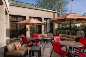 An outdoor patio area with a sofa, chairs, and tables, featuring striped umbrellas and a flag. - Hilton Garden Inn Phoenix Airport North (Phoenix)