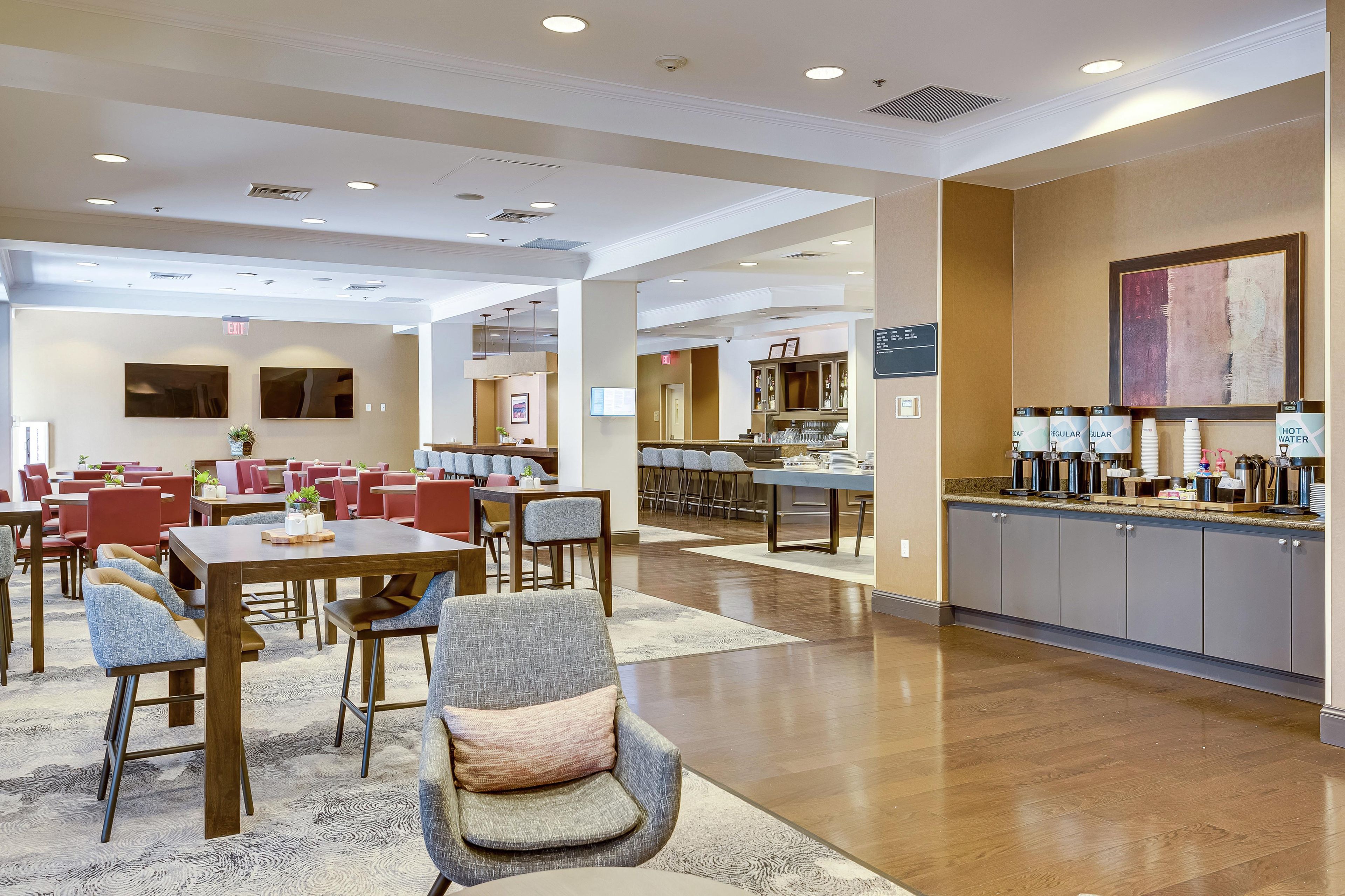 A hotel lobby with multiple dining areas, a reception desk, and a coffee station.