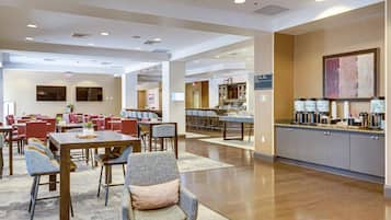 A hotel lobby with multiple dining areas, a reception desk, and a coffee station.