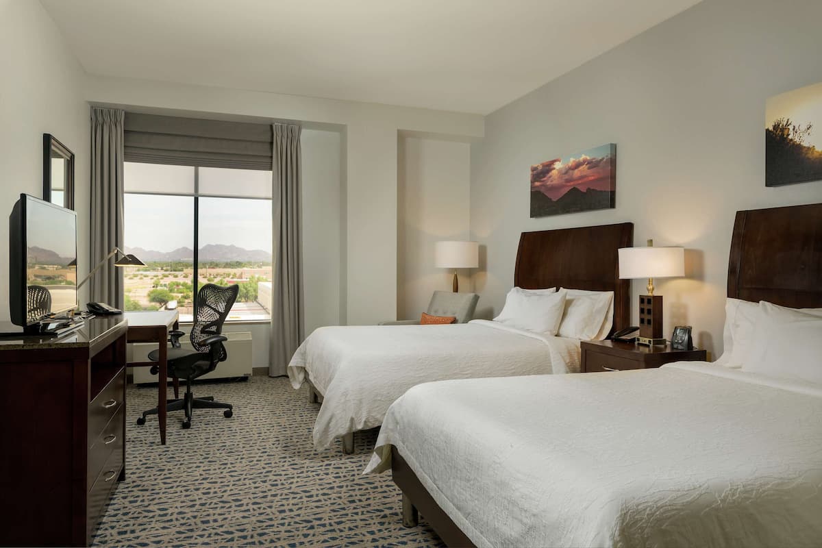 A hotel room with two beds, a desk with a computer, a chair, and a view of the mountains.