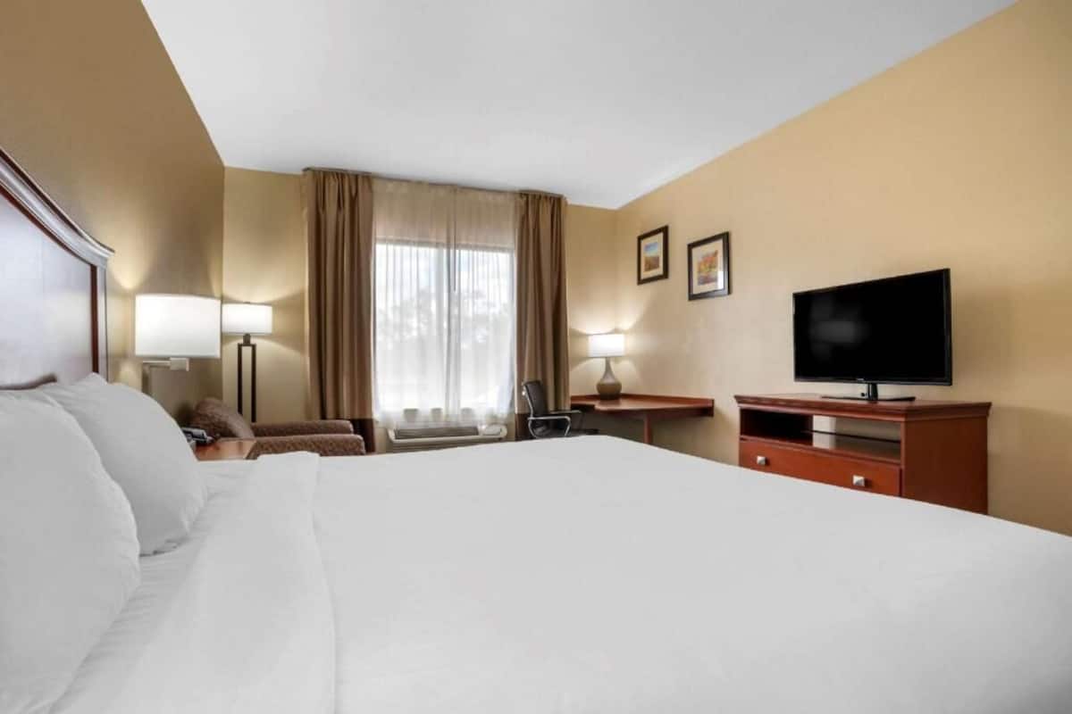 Une chambre d’hôtel avec un grand lit, un bureau avec une télévision, une chaise et une fenêtre avec des rideaux.