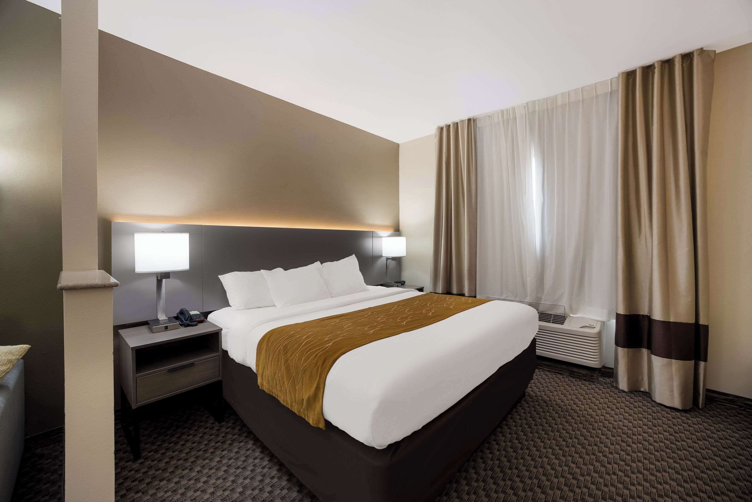 A hotel room with a large bed, a nightstand, a lamp, and a window with curtains.
