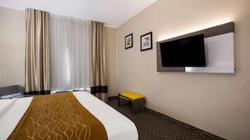 Ein Hotelzimmer mit einem Bett, einem an der Wand befestigten Fernseher, einem kleinen Hocker und Vorhängen.