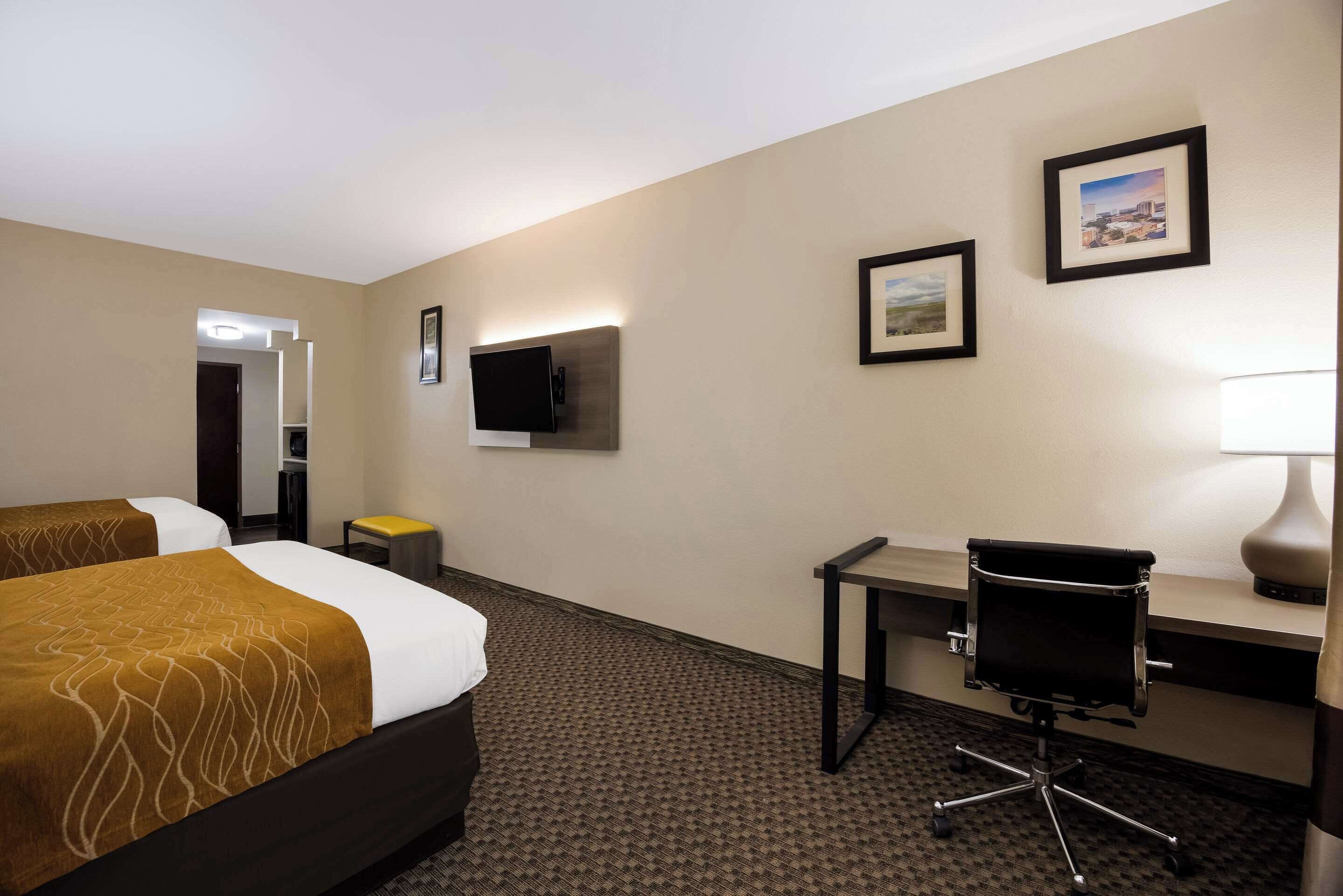A hotel room with two beds, a desk, a chair, a TV, and framed pictures on the wall.