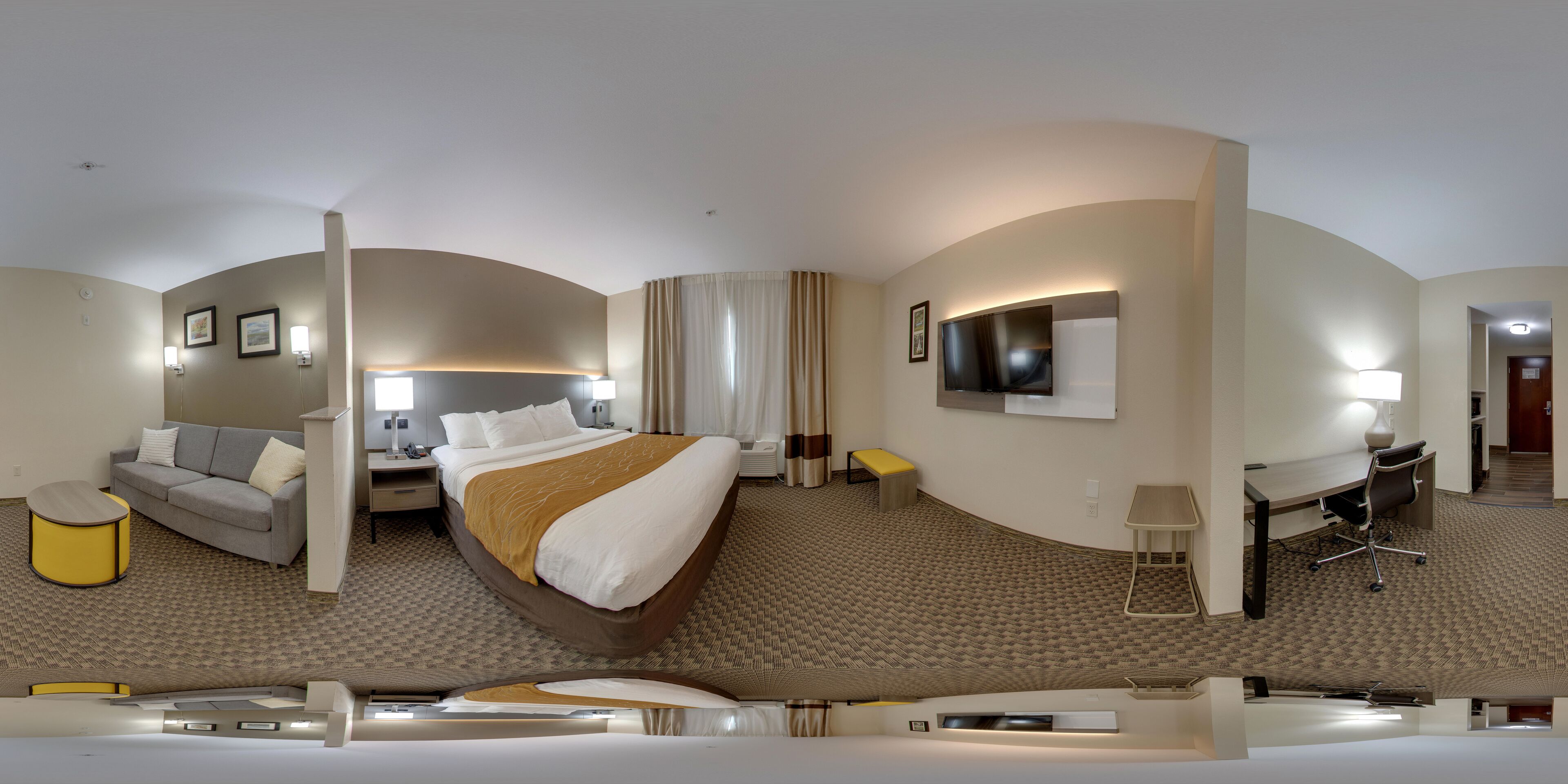 A hotel room with a curved bed, a sofa, a desk, and a TV.