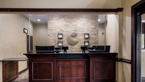 A reception desk with a stone wall backdrop, a large mirror above, and two phone stations. - Comfort Inn & Suites Midway - Tallahassee West (Midway)