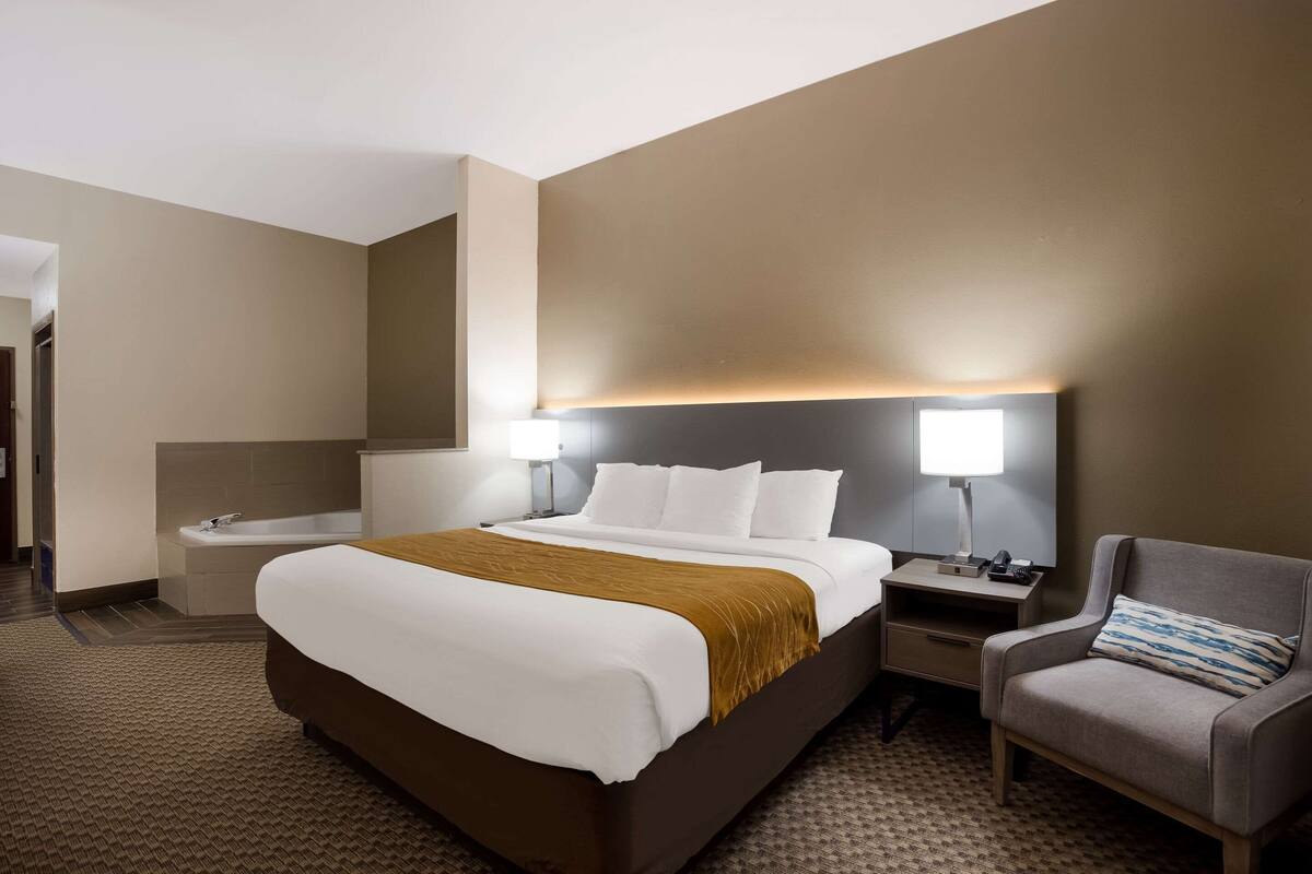 Une chambre d’hôtel avec un grand lit, une table de chevet, une chaise et une salle de bain avec une baignoire.
