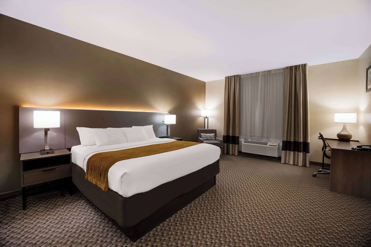 Une chambre d’hôtel avec un grand lit, deux tables de chevet avec des lampes, un bureau avec une chaise et une fenêtre avec des rideaux.
