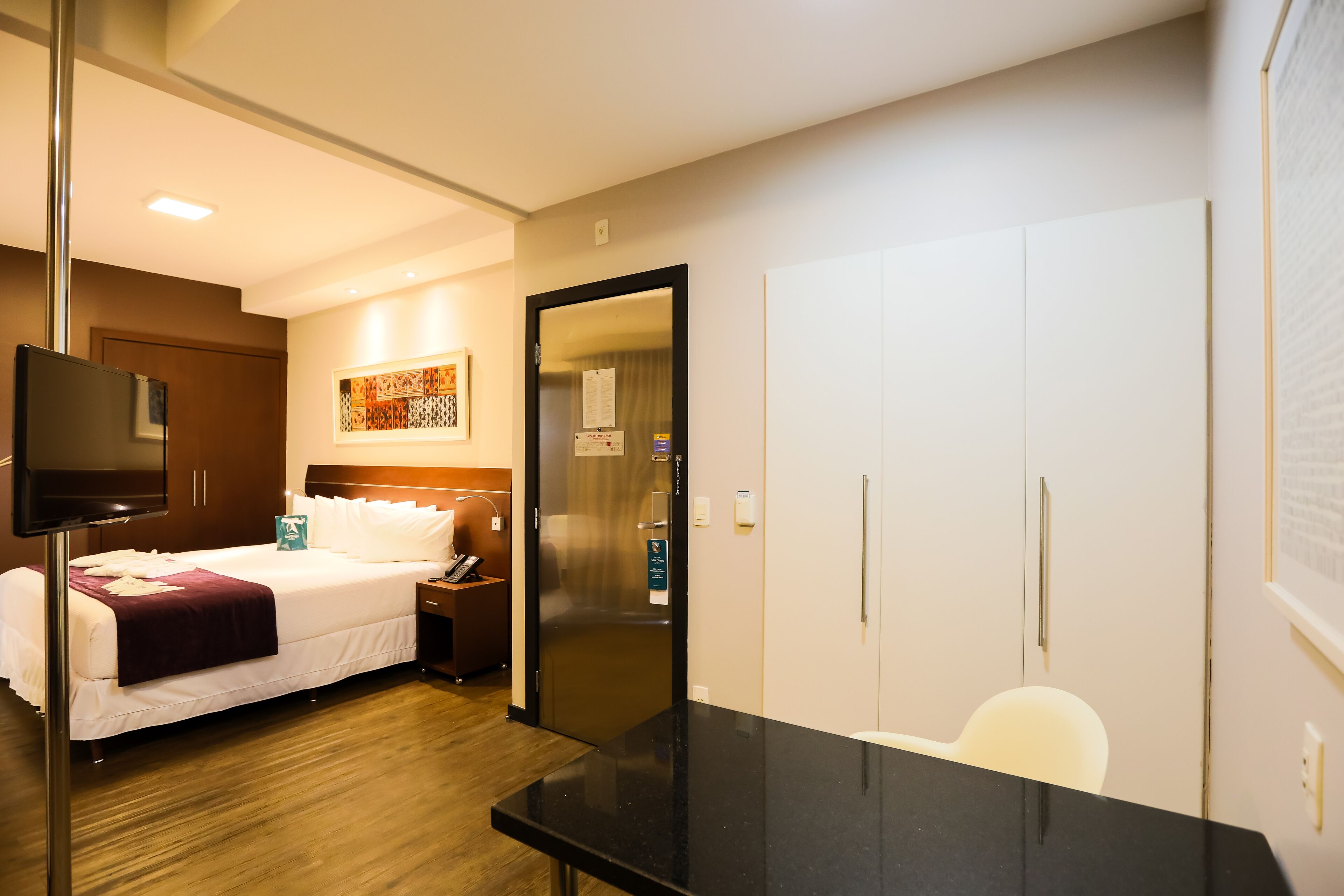 A hotel room with a bed, a desk, a chair, a TV, and a wardrobe.