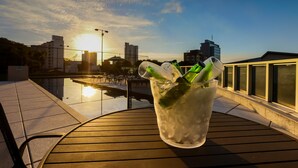 Ein Tisch mit einem Getränk im Glas, mit Blick auf eine Stadtlandschaft mit Gebäuden und einem Gewässer.