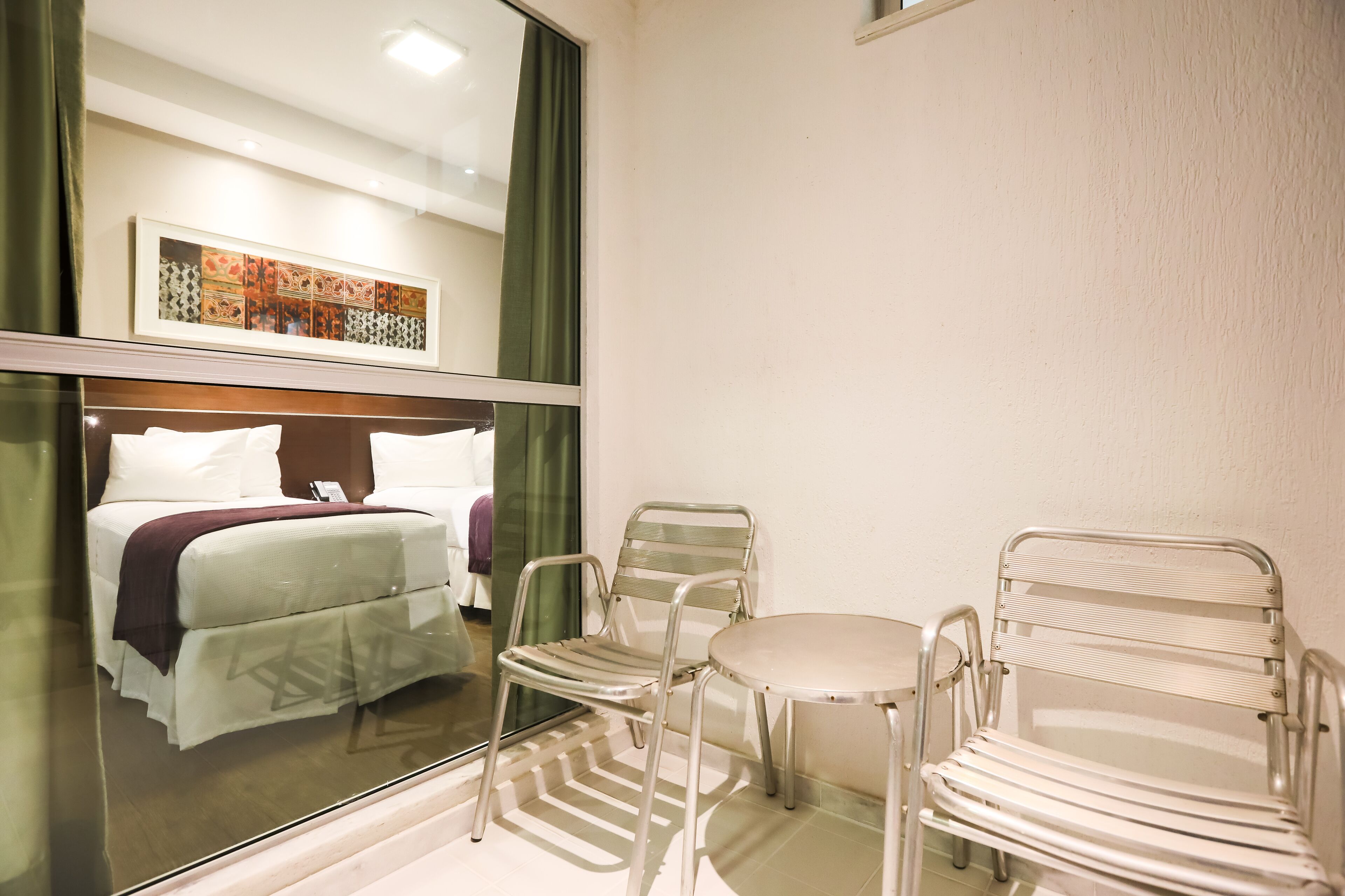 Hotellihuone, jossa on sänky, kaksi tuolia, pieni pöytä ja suuri ikkuna.