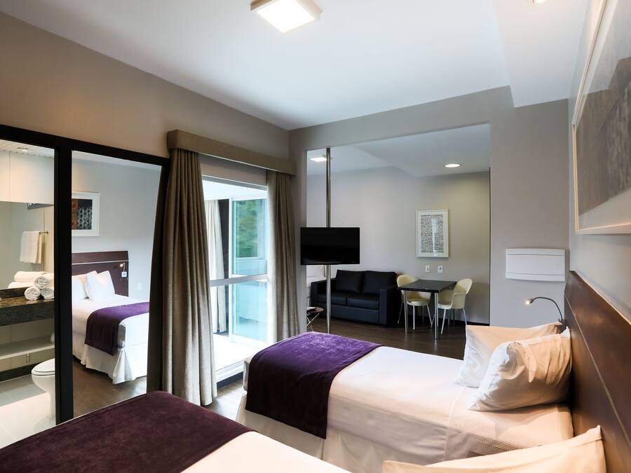 A hotel room with two beds, a TV, a desk, and a view of the outdoors.