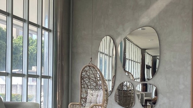 Ein modernes Interieur mit einem großen Fenster, einem Korbstuhl, einem runden Tisch und einer Couch.