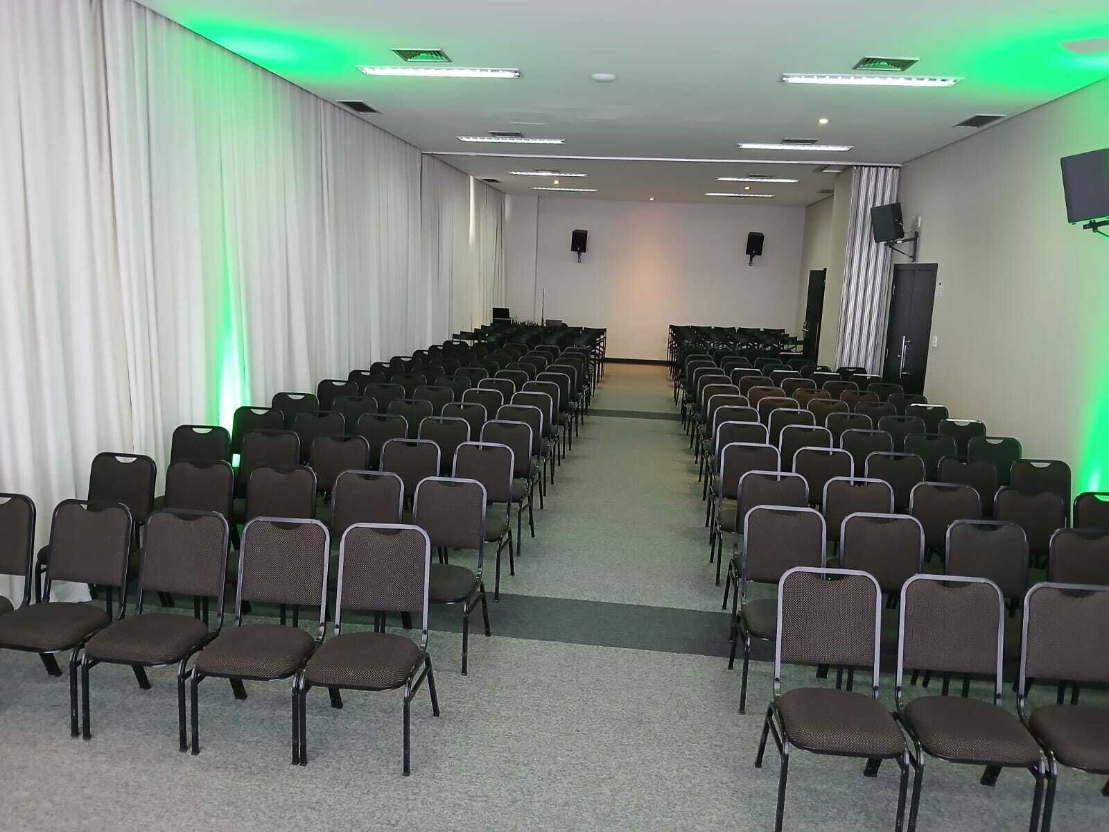 A conference room with rows of chairs, a stage, and a projector screen.