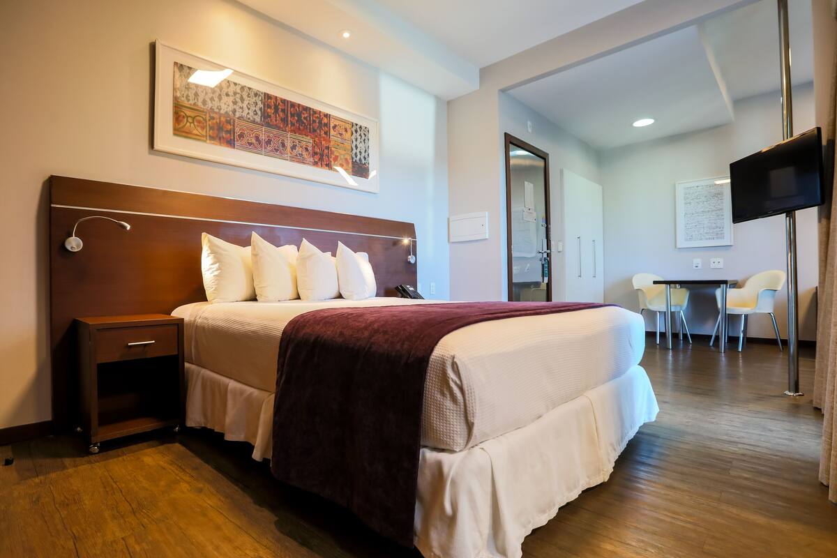 A hotel room with a large bed, a nightstand, a desk with a chair, and a television.