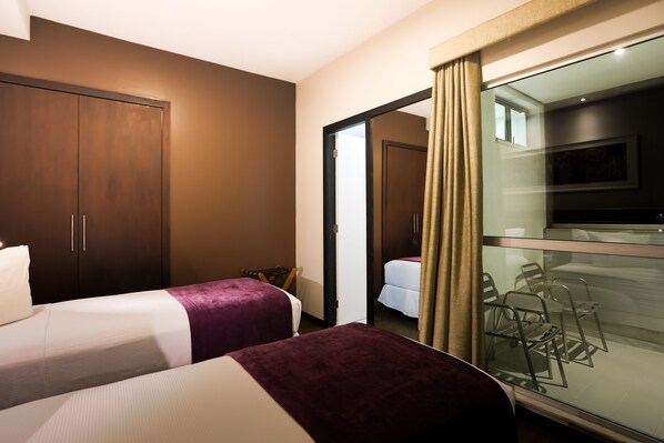 A hotel room with two beds, a wardrobe, a glass partition, and a small seating area.