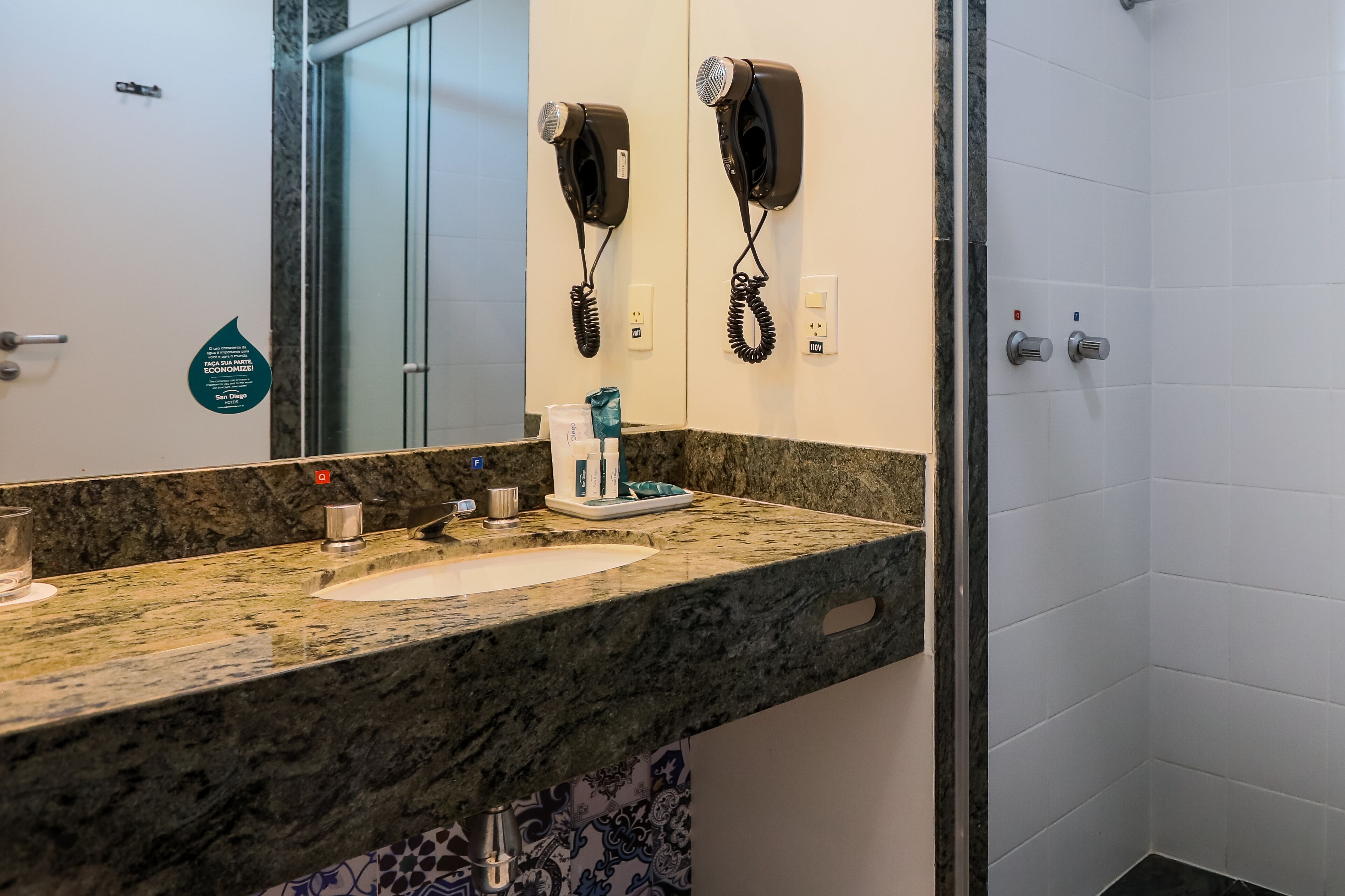 A bathroom with a granite countertop, a sink, a mirror, and two hair dryers mounted on the wall.