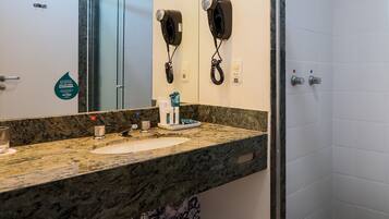 A bathroom with a granite countertop, a sink, a mirror, and two hair dryers mounted on the wall.