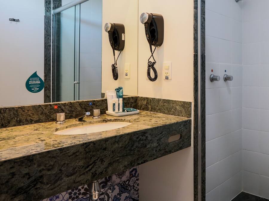 A bathroom with a granite countertop, a sink, a mirror, and two hair dryers mounted on the wall.