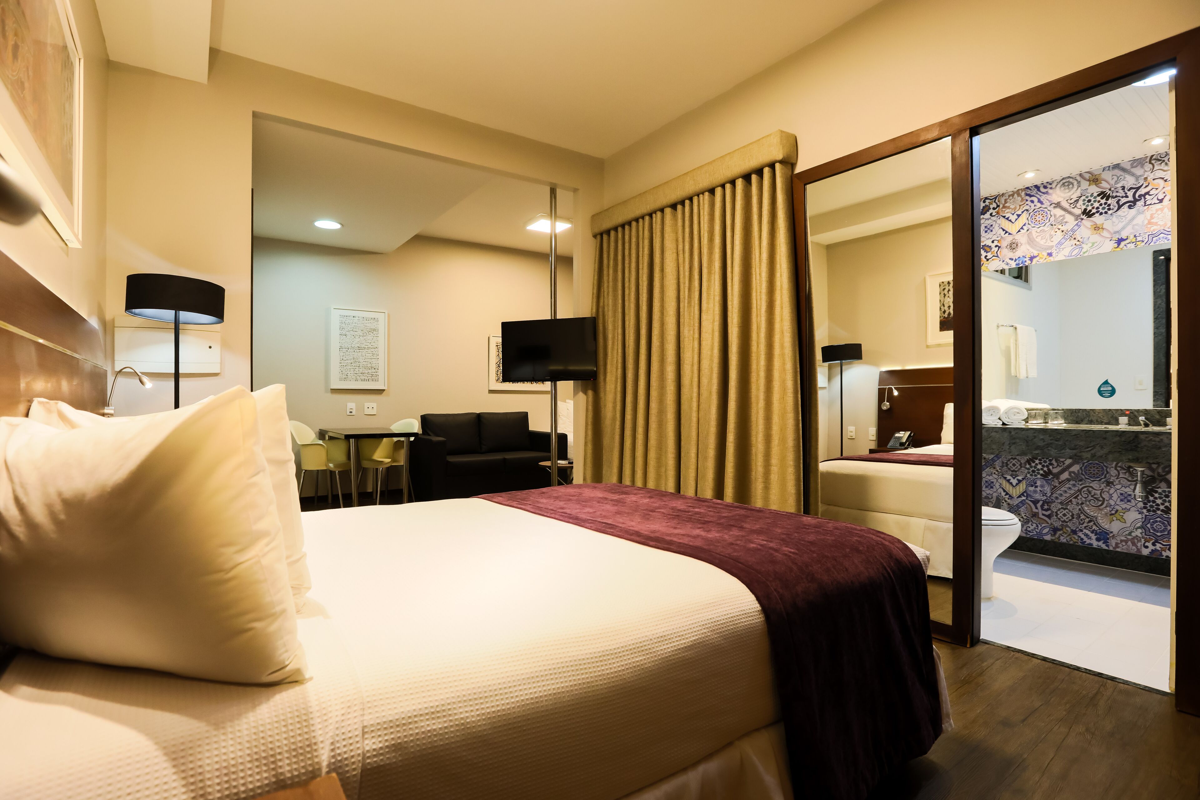 Ein Hotelzimmer mit einem großen Bett, einem Schreibtisch, einem Stuhl, einem Fernseher und einem durch eine offene Tür einsehbaren Badezimmer.
