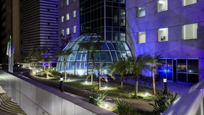 Ein modernes Hotel mit einem Glasatrium, Palmen und einem gut beleuchteten Außenbereich.