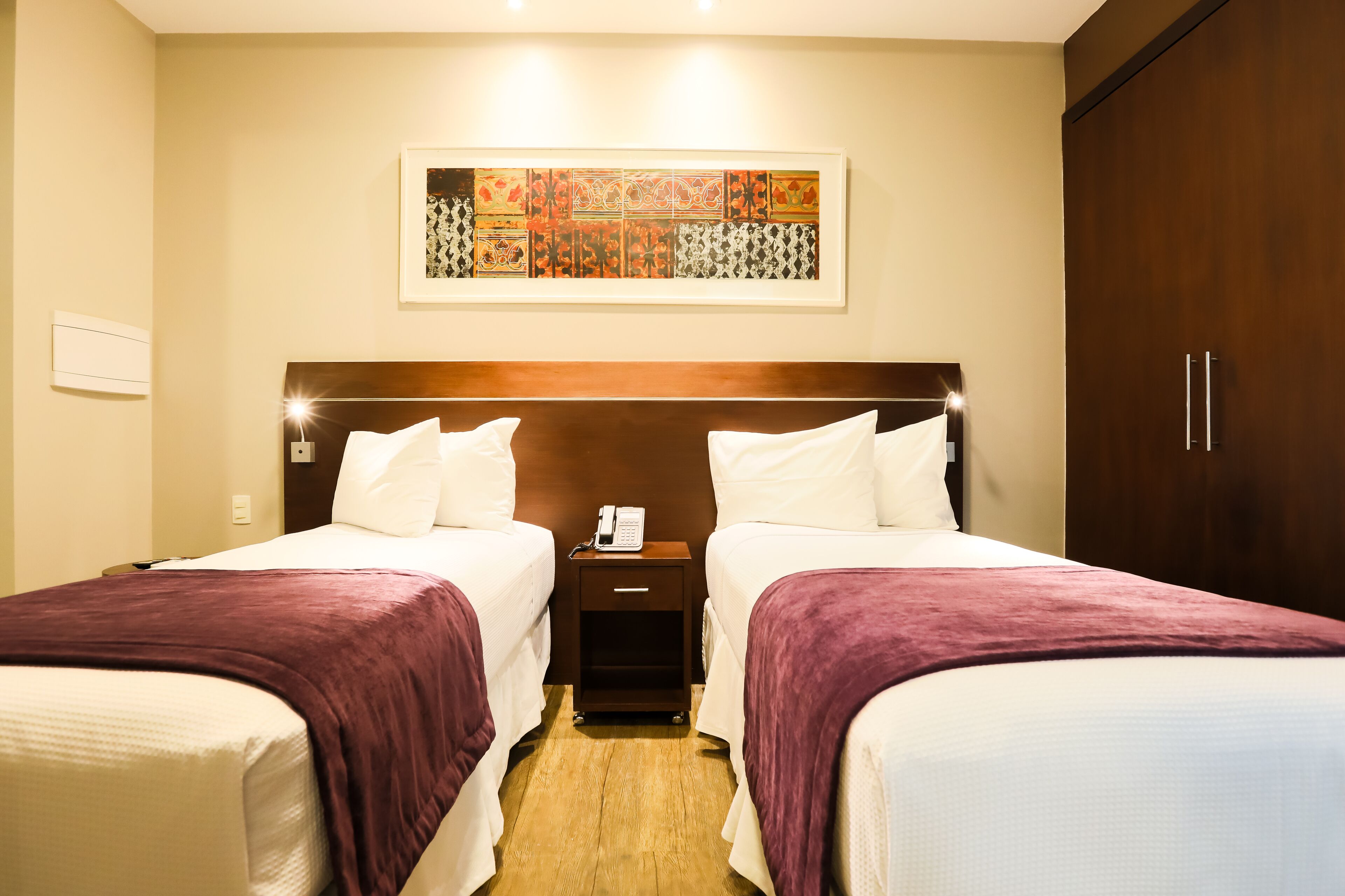 A hotel room with two beds, a wooden headboard, a nightstand with a phone, and a large abstract painting on the wall.