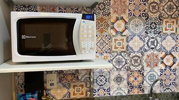 Uma cozinha com micro-ondas branco numa prateleira, uma pia e bancada de mármore.
