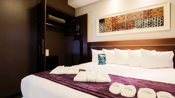 A hotel room with a neatly made bed, a large artwork on the wall, and a closet with a mirror.