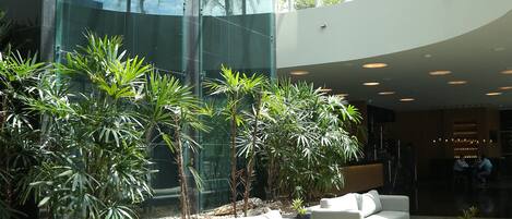 A spacious lobby with a modern glass facade, a white sofa, and several potted plants.