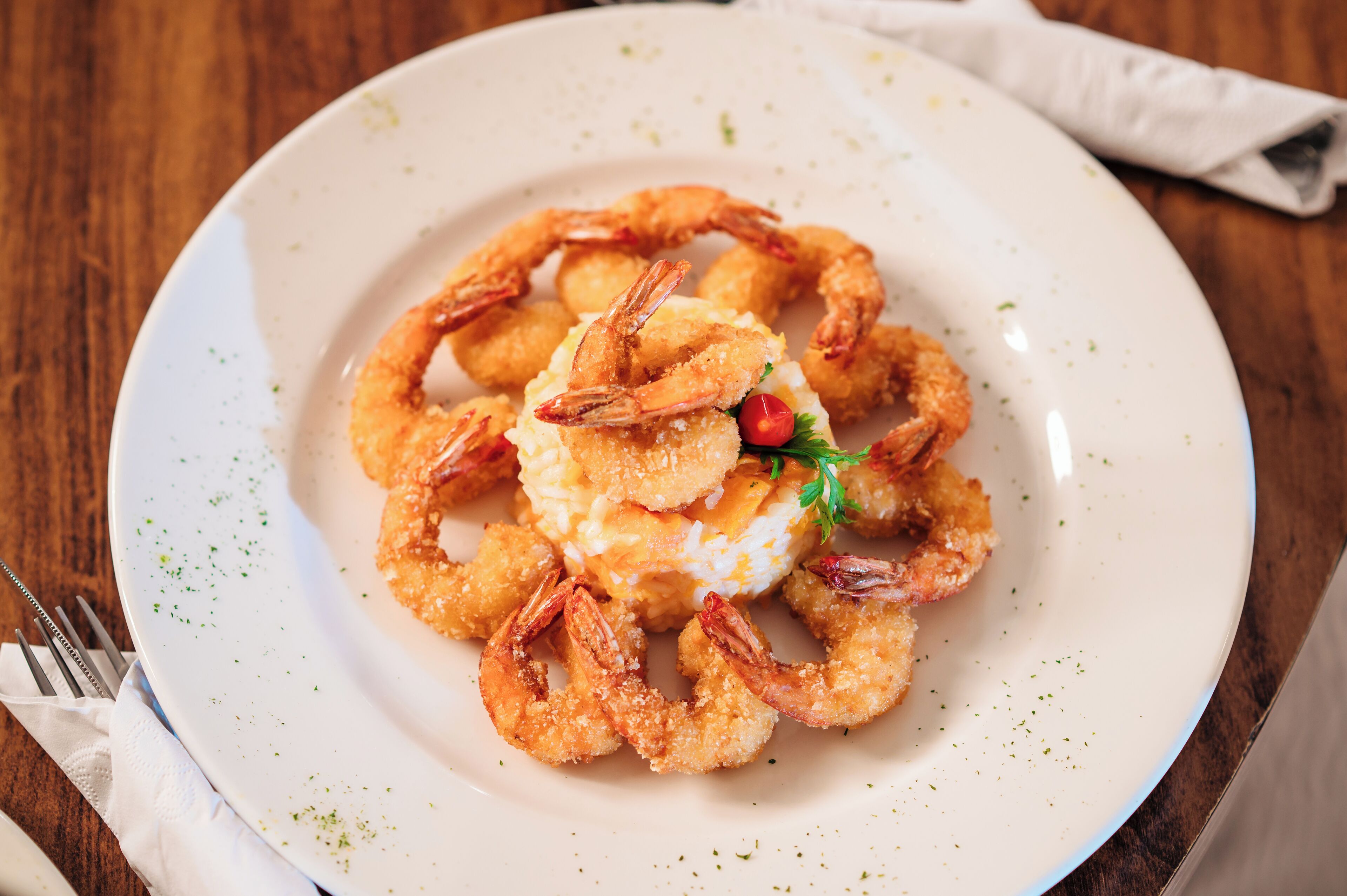 Prato de camarões fritos e pamonha, com guarnição, servido em prato branco.