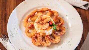 Prato de camarões fritos e pamonha, com guarnição, servido em prato branco.