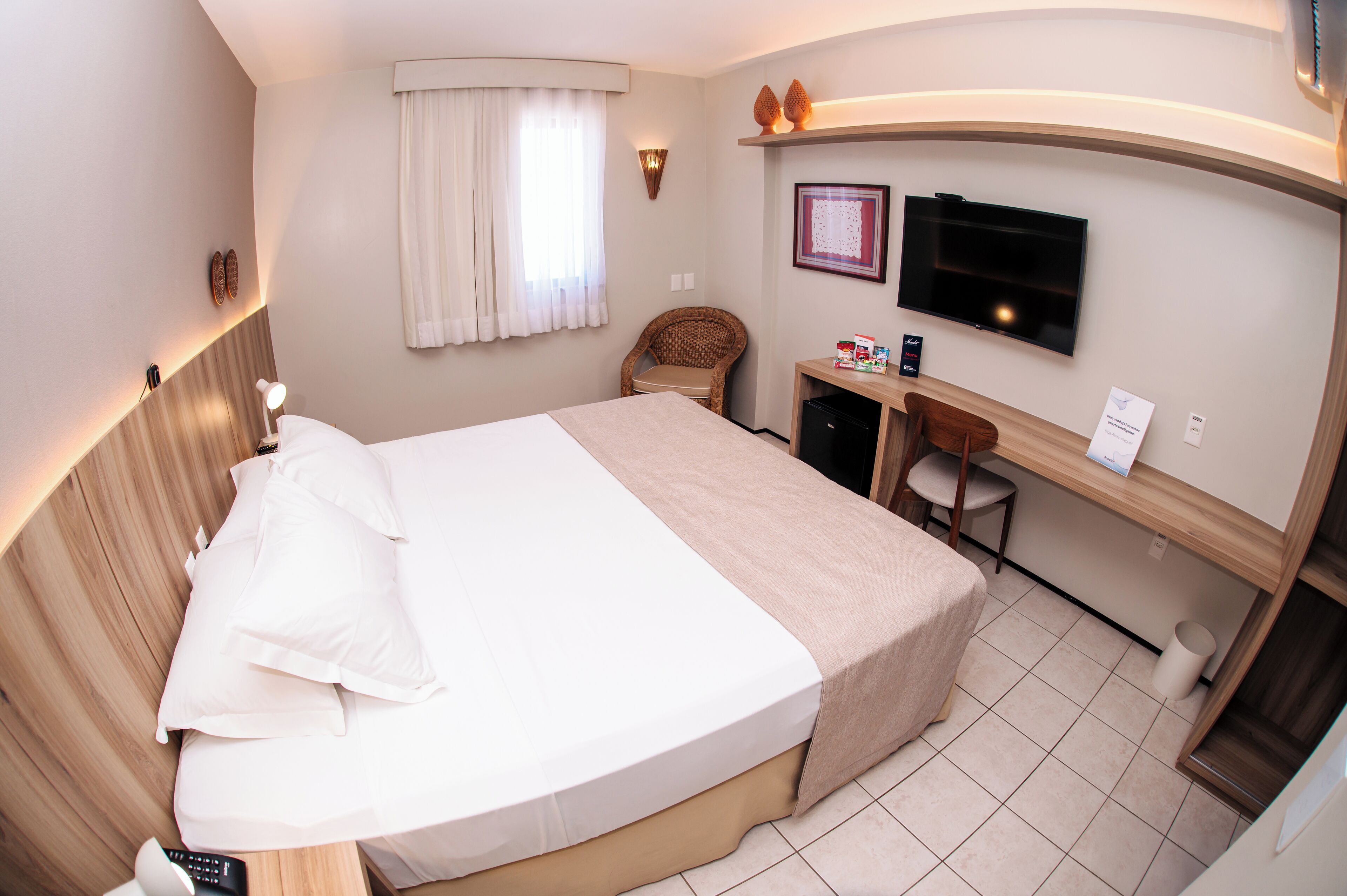 Una habitación de hotel con cama, escritorio, silla, televisión y ventana con cortinas.