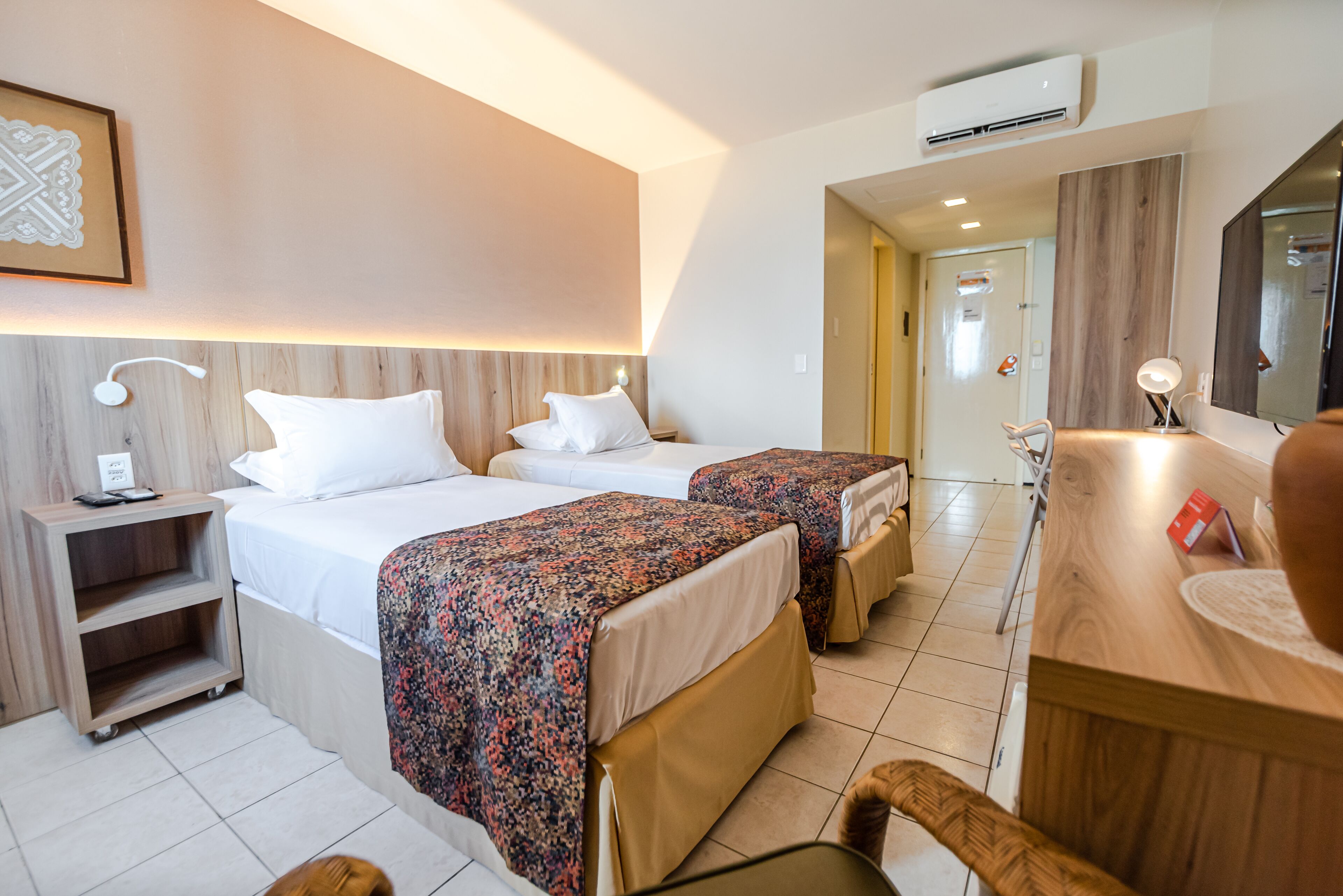 A hotel room with two beds, a desk, a chair, and a mirror.