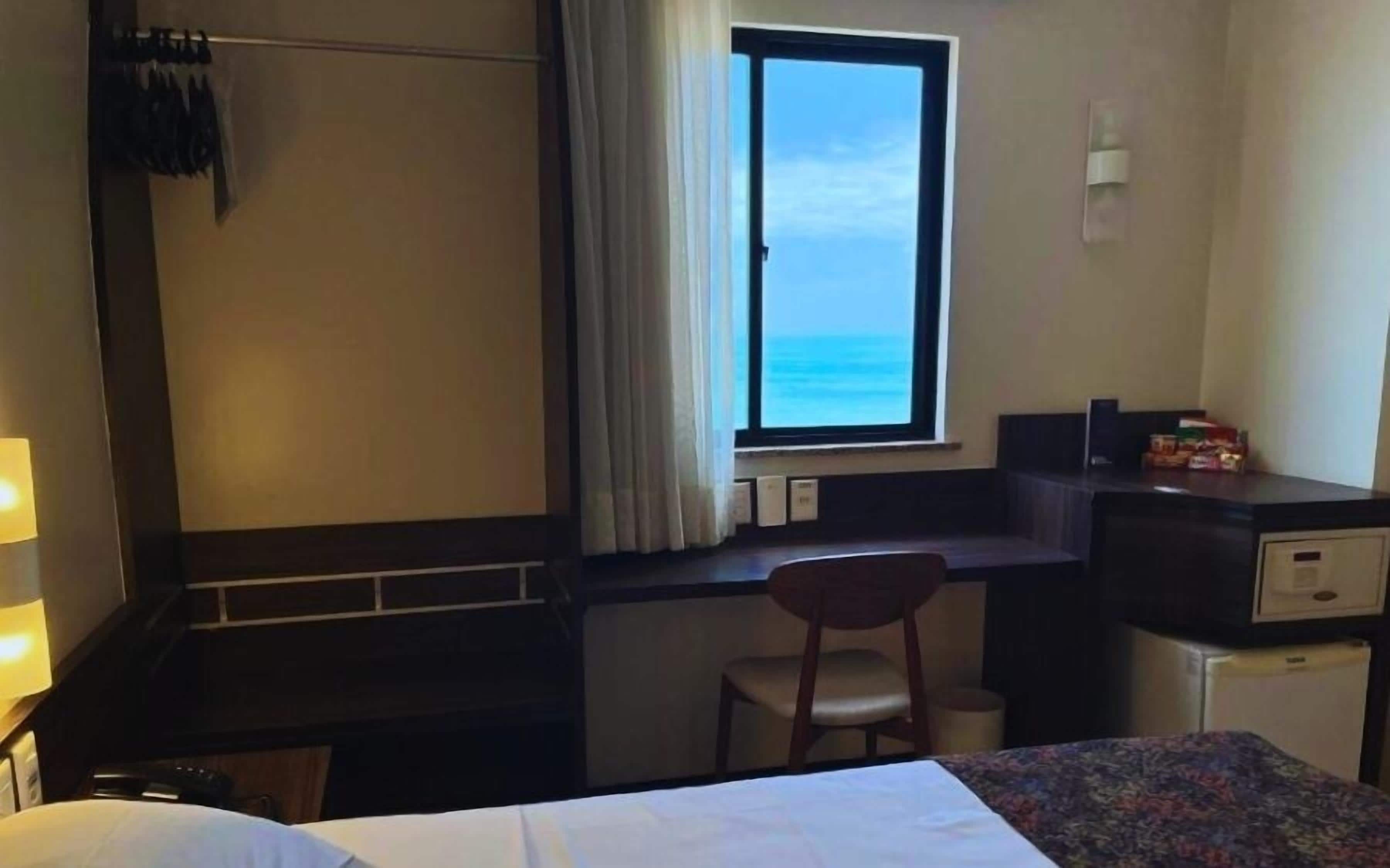 Habitación de hotel con cama, escritorio, silla y ventana con vista al océano.