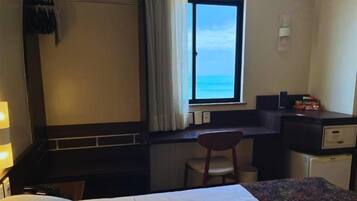 Habitación de hotel con cama, escritorio, silla y ventana con vista al océano.