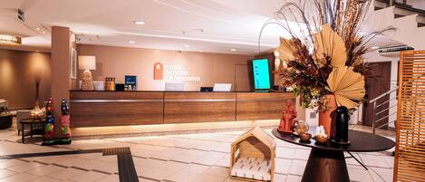 A hotel reception area with a wooden reception desk, a small dog house, and a decorative plant arrangement.
