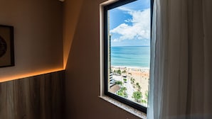 Una habitación con un ventanal grande que da a una playa, un cuadro enmarcado en la pared y un diseño de paneles de madera.