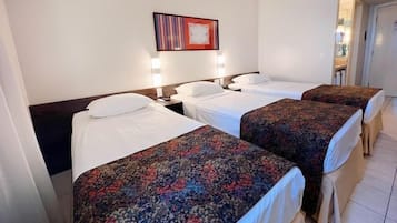 Habitación de hotel con tres camas individuales, cada una con una colcha estampada, una mesita de noche y una lámpara de pared.