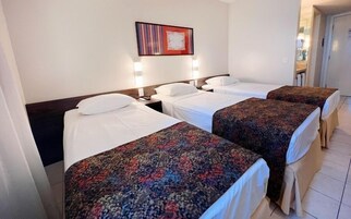 Habitación de hotel con tres camas individuales, cada una con una colcha estampada, una mesita de noche y una lámpara de pared.