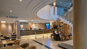 Una hall d'hotel moderna con una reception, un'area salotto e una scala che conduce a un piano superiore.