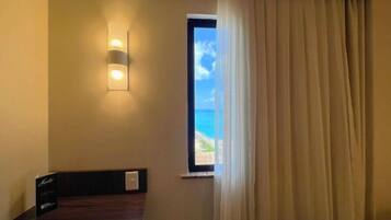 A hotel room with a view of the beach, a bedside table, and a wall-mounted light fixture.