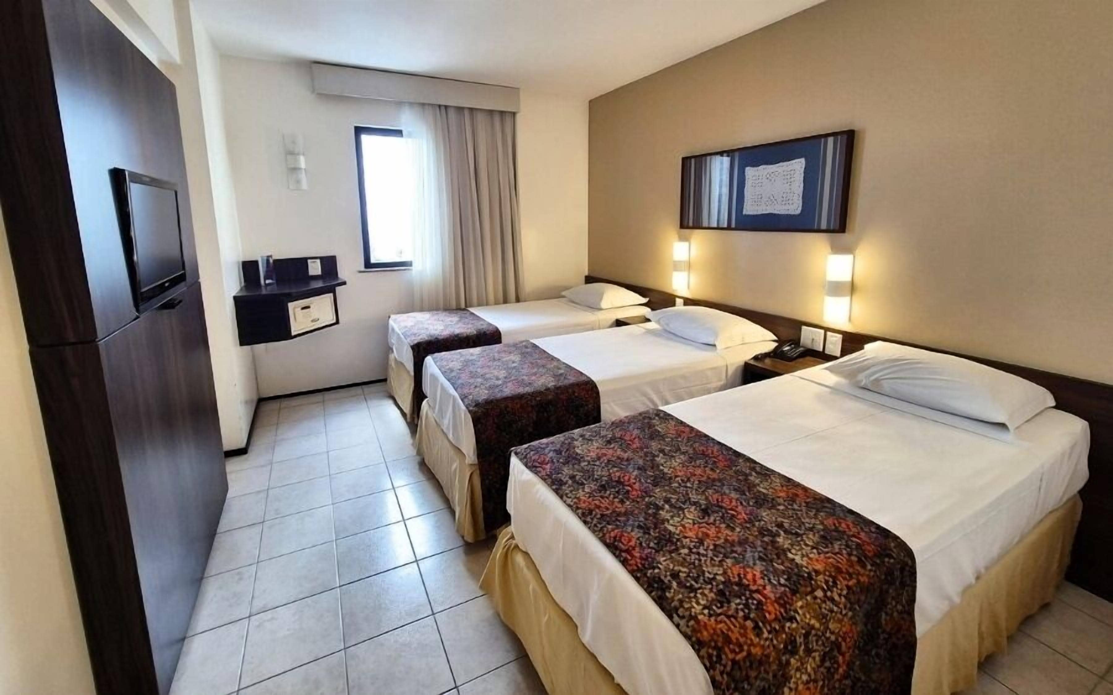 A hotel room with two beds, a desk, a TV, and a window with curtains.