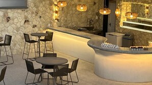 Zona bar con pareti in pietra, tavoli e sedie rotonde, un bancone con esposizione illuminata e lampade in vimini a sospensione.