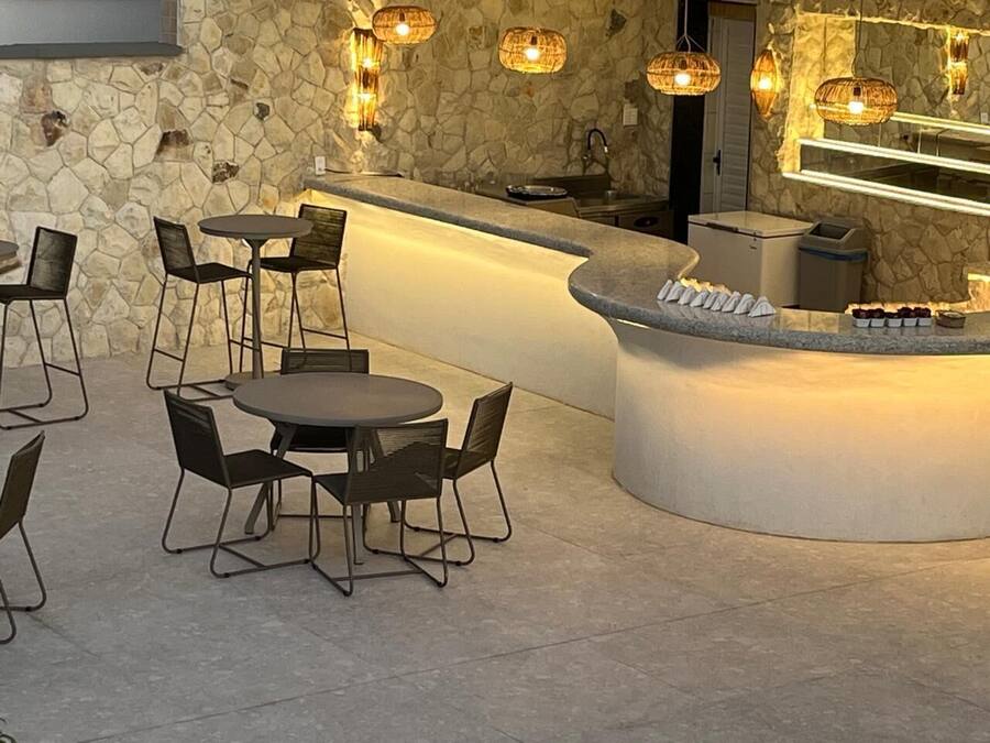 Zona de bar con paredes de piedra, mesas y sillas redondas, una barra con vitrina iluminada y lámparas de mimbre colgantes.