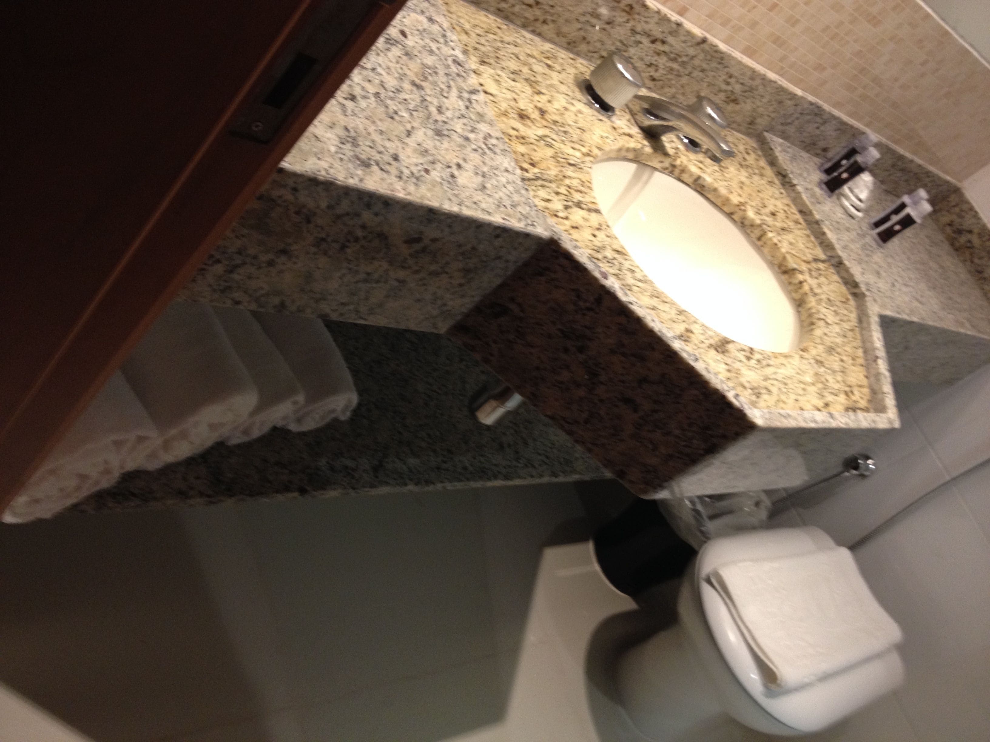 A bathroom with a granite countertop, a sink, a toilet, and a towel rack.