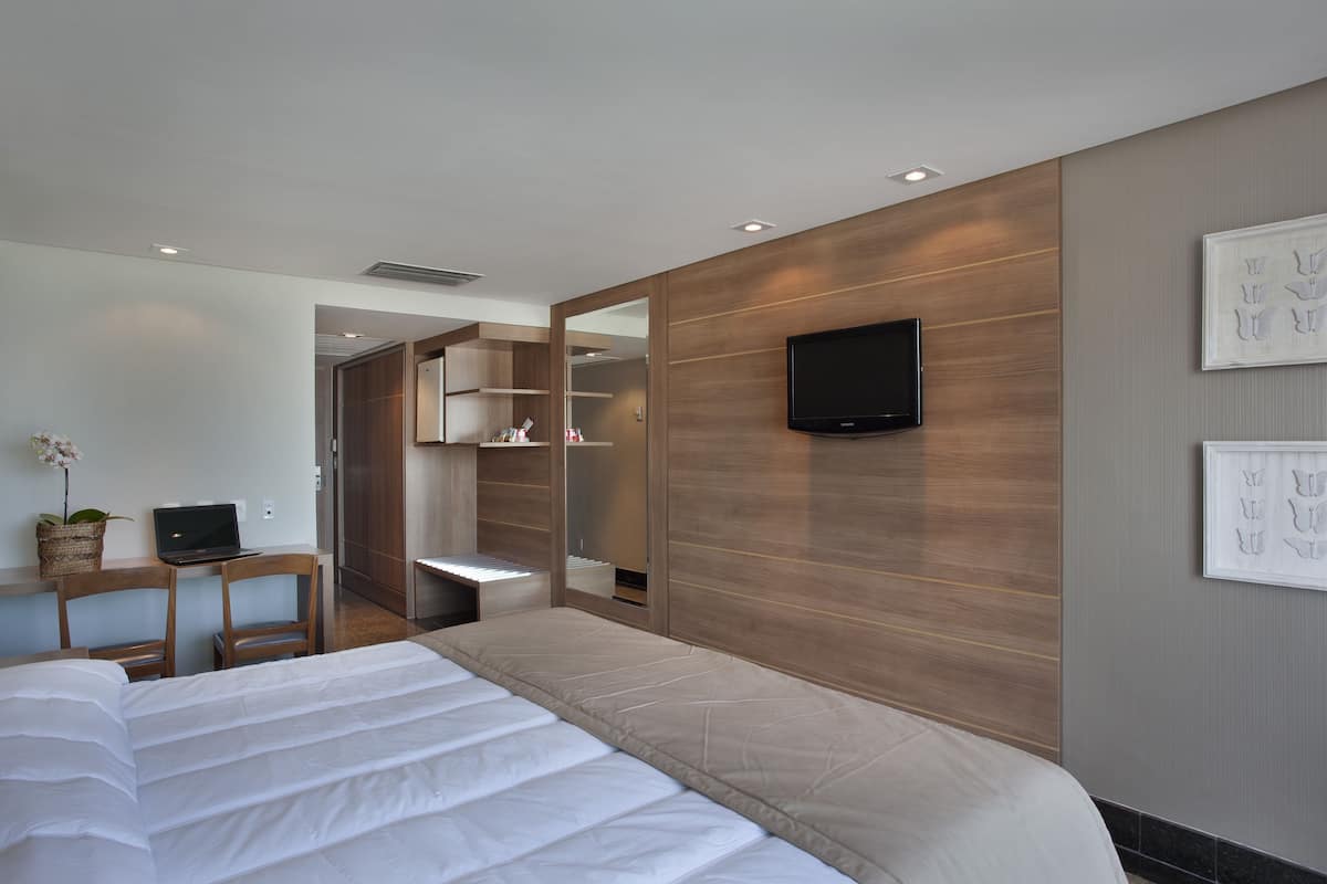Une chambre d’hôtel moderne dotée d’un grand lit, d’un bureau avec un ordinateur portable, d’un téléviseur fixé au mur et d’un miroir.