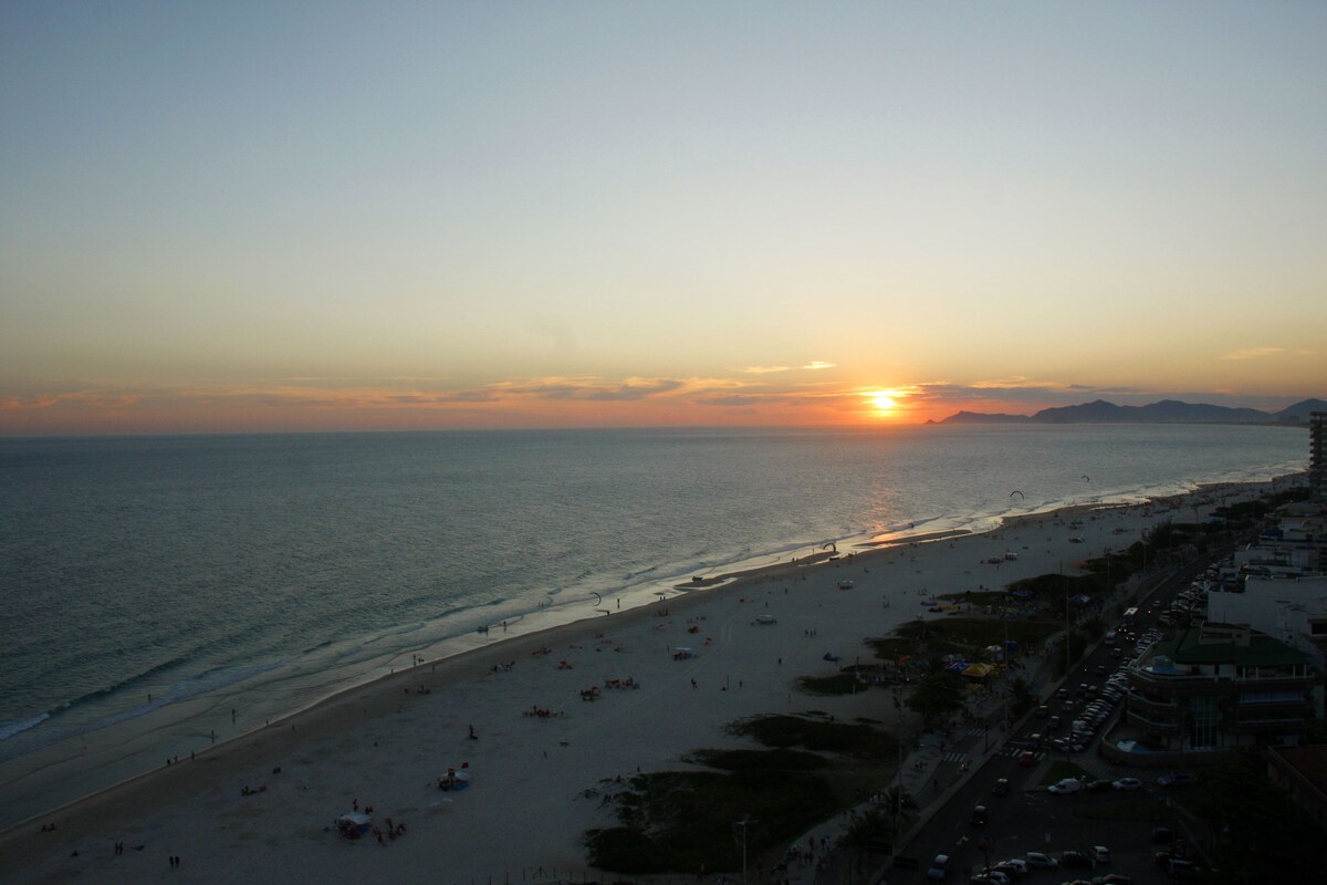 Ein Strand mit Sonnenuntergang, einer Straße und Gebäuden entlang der Küste.