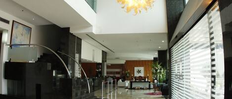 A modern lobby with a central staircase, a large chandelier, and a reception desk.