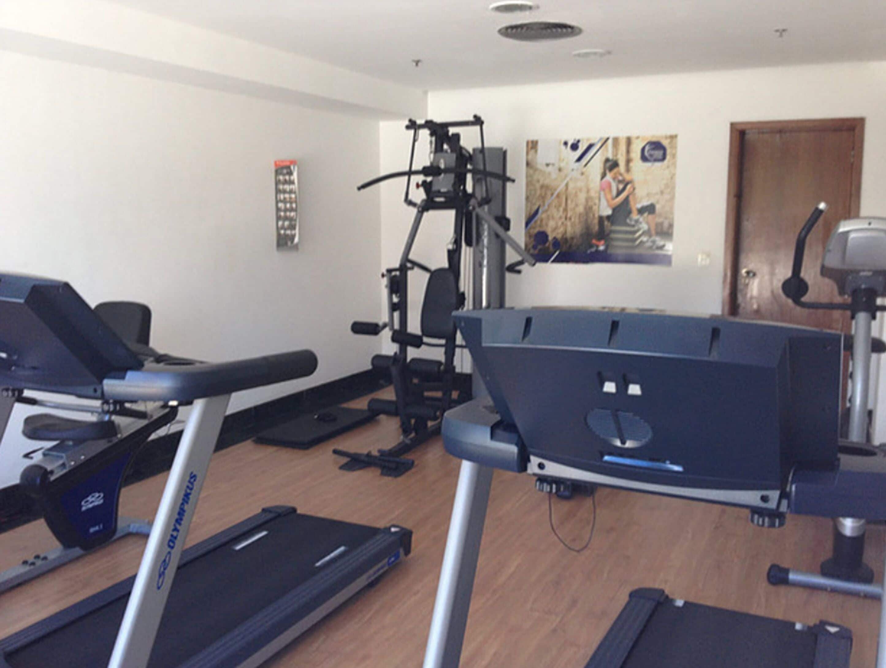 Un gimnasio con cintas de correr, máquinas de pesas y un cartel en la pared.