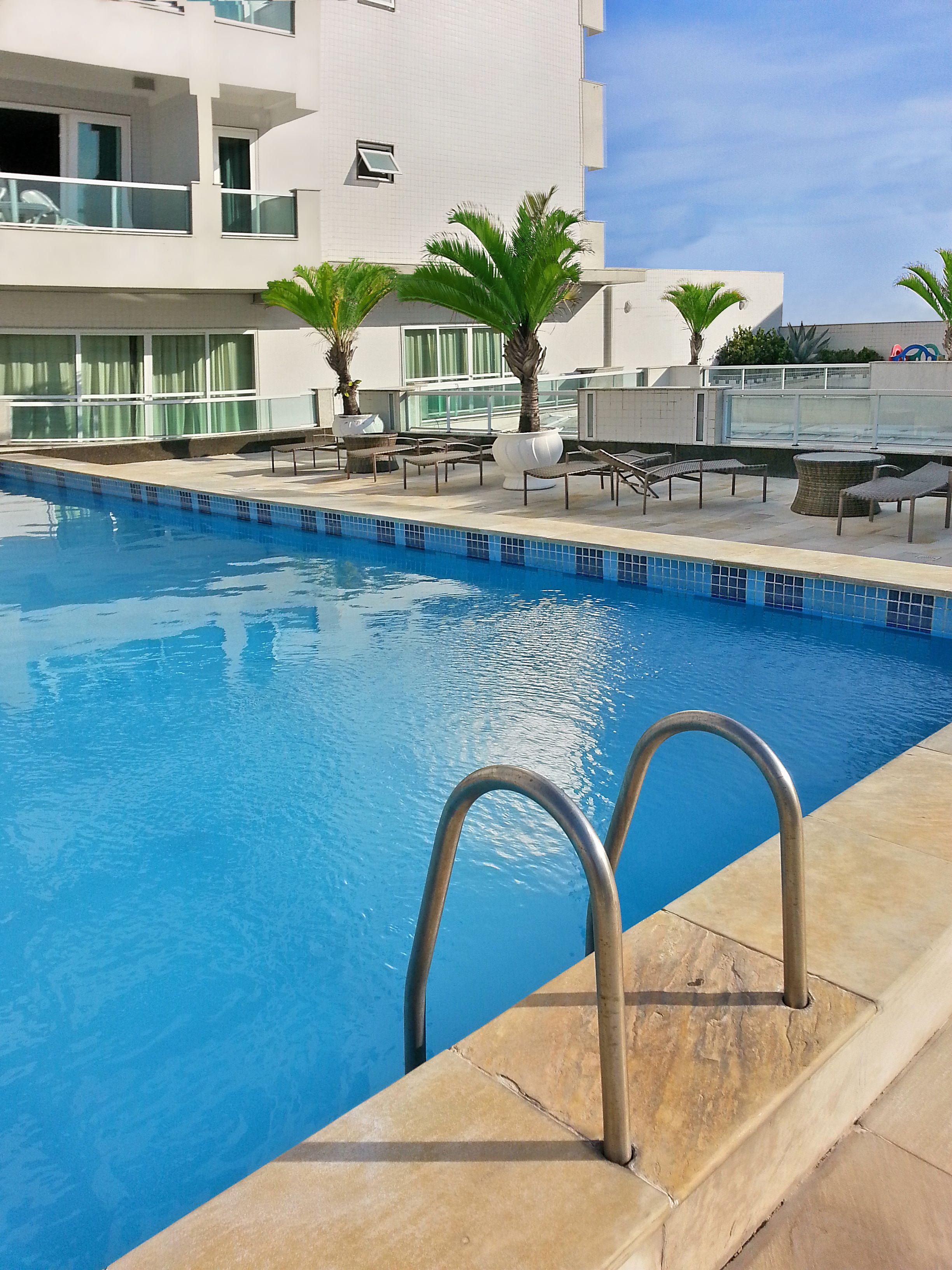 A swimming pool with a clear blue water, surrounded by lounge chairs and palm trees.